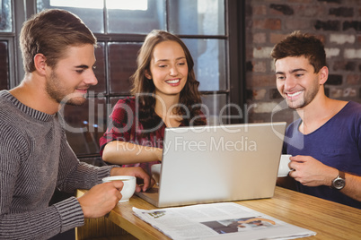 Smiling friends drinking coffee and looking at laptop