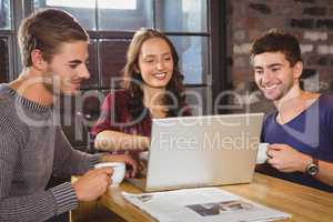 Smiling friends drinking coffee and looking at laptop