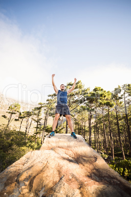 Young happy jogger standing on rock and cheering