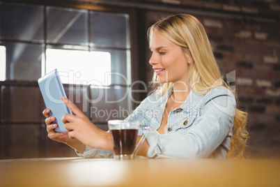 Smiling blonde having coffee and looking at tablet computer