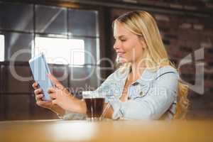 Smiling blonde having coffee and looking at tablet computer
