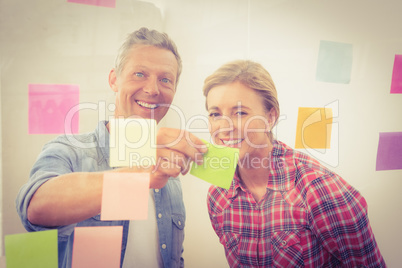 Smiling casual businessman showing sticky note to colleague