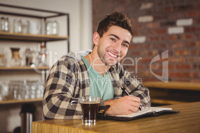 Smiling hipster having coffee and writing in planner