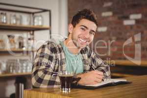 Smiling hipster having coffee and writing in planner