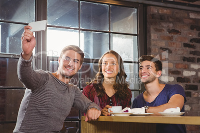 Smiling friends having coffee and taking selfies