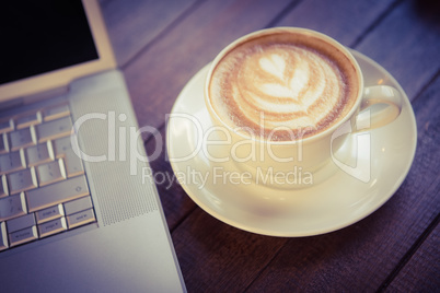 Cup of cappuccino with coffee art next to laptop