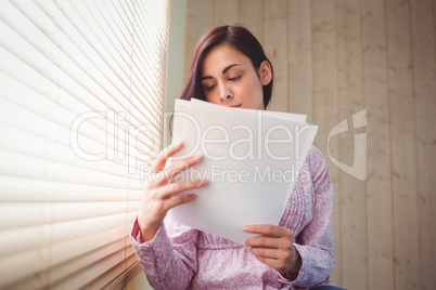 Pretty brunette reading documents beside window