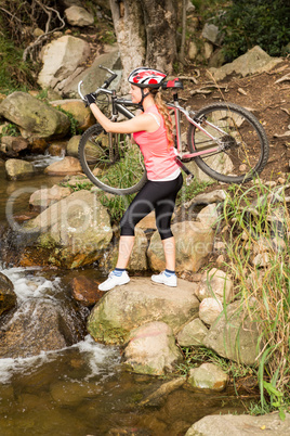 Blonde athlete carrying her mountain bike over stream