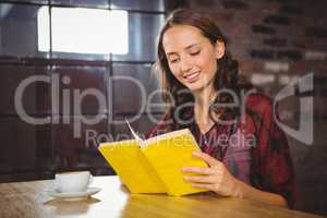 Smiling brunette turning the page of yellow book