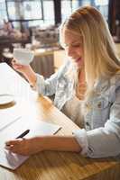 Smiling blonde drinking coffee and writing on sheet of paper