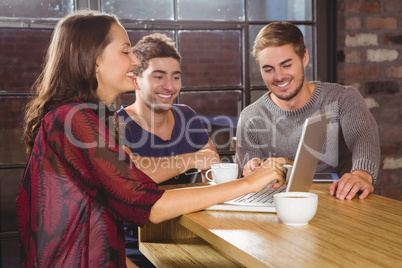 Smiling friends having coffee together and looking at laptop