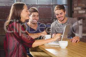 Smiling friends having coffee together and looking at laptop