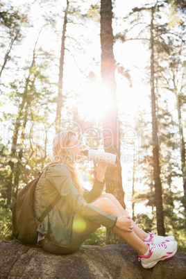 Pretty blonde hiker drinking and sitting on stone