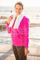 Smiling sporty woman with water bottle listening to music
