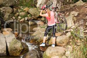 Blonde athlete carrying her mountain bike over stream