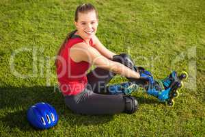 Smiling sporty blonde skater sitting in grass