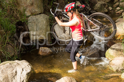 Blonde athlete carrying her mountain bike over stream