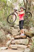 Blonde athlete carrying her mountain bike over rocks