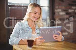 Smiling blonde having coffee and using tablet computer