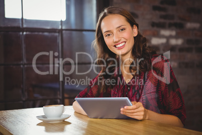 Smiling brunette having coffee and holding tablet