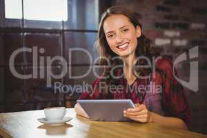 Smiling brunette having coffee and holding tablet