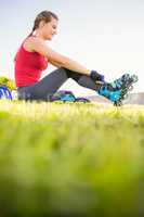 Smiling sporty blonde skater sitting in grass