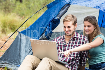 Young pretty hiker couple sitting in a tent looking at laptop