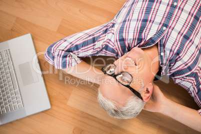 Smiling man lying on floor next to laptop