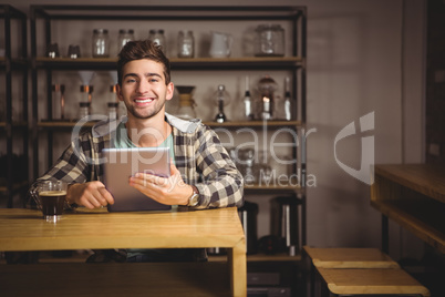 Smiling hipster having coffee and holding tablet computer