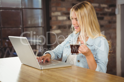 Smiling woman drinking coffee and typing on laptop