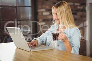 Smiling woman drinking coffee and typing on laptop