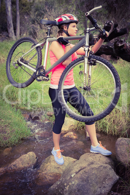 Blonde athlete carrying her mountain bike over stream