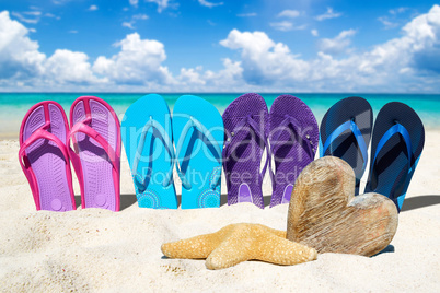 Flip Flops in einer Reihe und Holzherz am Sandstrand