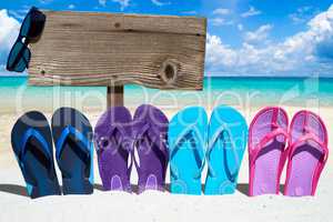 Bunte Flip Flops und ein Holzschild mit Textfreiraum am Strand