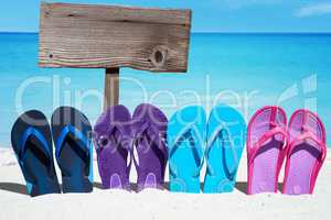 Bunte Flip Flops und ein Holzschild mit Textfreiraum am Strand