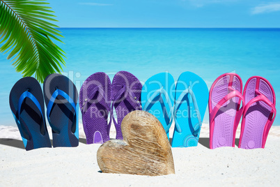 Bunte Flip Flops und ein Herz aus Holz am Sandstrand