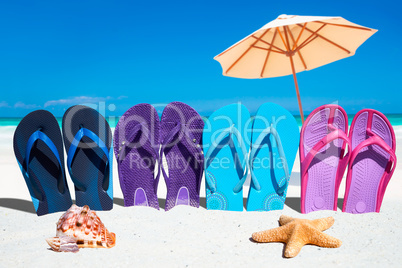 Bunte Flip Flops in einer Reihe mit Muscheln und Sonnenschirm