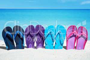 Eine Reihe bunter Flip Flops stecken im Sand am Badestrand