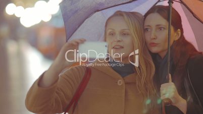 Two women friends making selfie with umbrella on rainy day