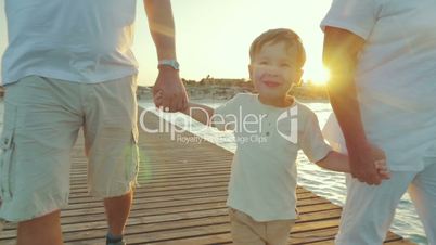 Happy boy walking with grandparents along the pier at sunset