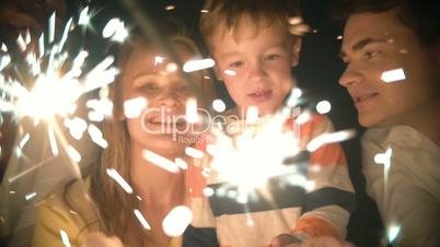Family of three holding sparklers and kissing
