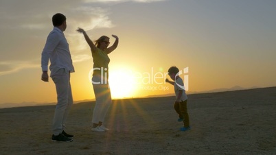 Happy family of three dancing on the beach at sunset