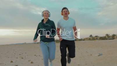 Young couple in headphones running on the beach