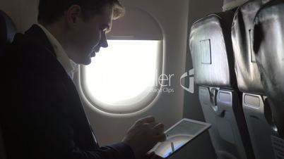 Young businessman working with pad in plane