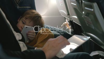Child with cell and and man using pad in plane