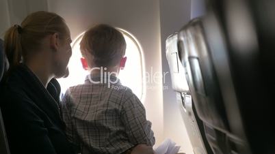 Mother and son looking out illuminator in plane