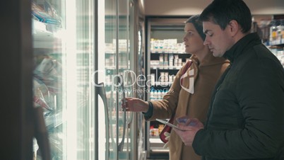 Young couple taking frozen food from fridge in the shop