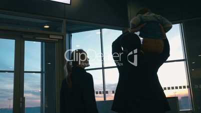 Young family looking out airport window at sunset