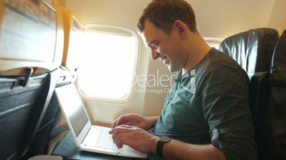 Young man chatting on laptop in the plane