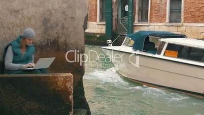 Woman working with laptop by the canal in Venice